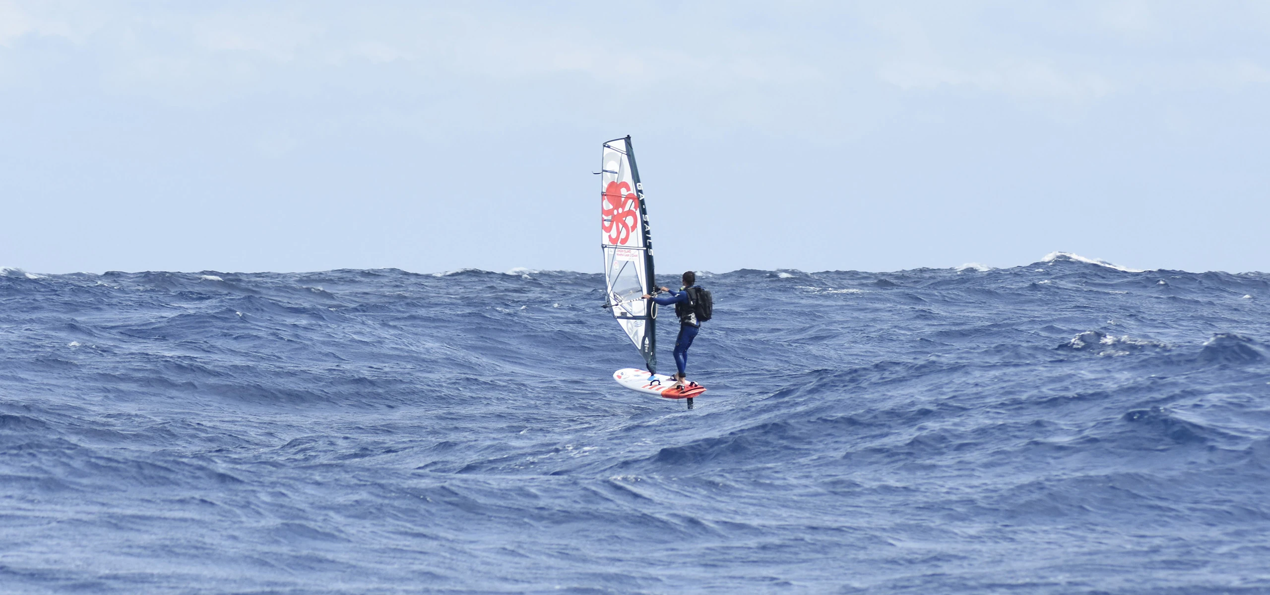 Jean-Christophe Le Gal en windfoil, de dos et seul au large, lors de sa traversée du continent vers la Corse